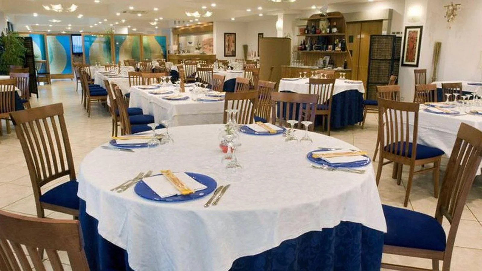 Sala ristorante con tavoli apparecchiati e tovaglie blu e bianche
