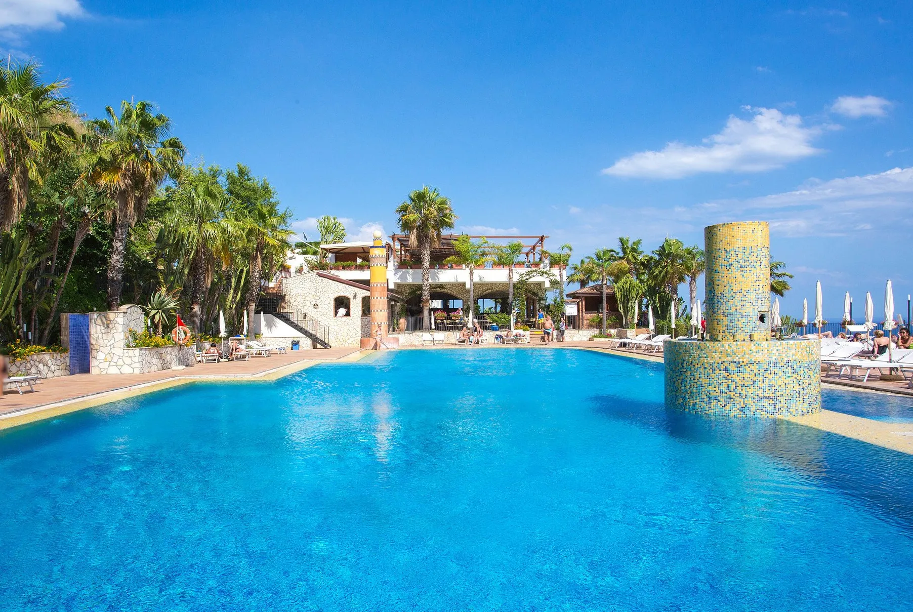 Grande piscina esterna con colonne a mosaico circondata da palme
