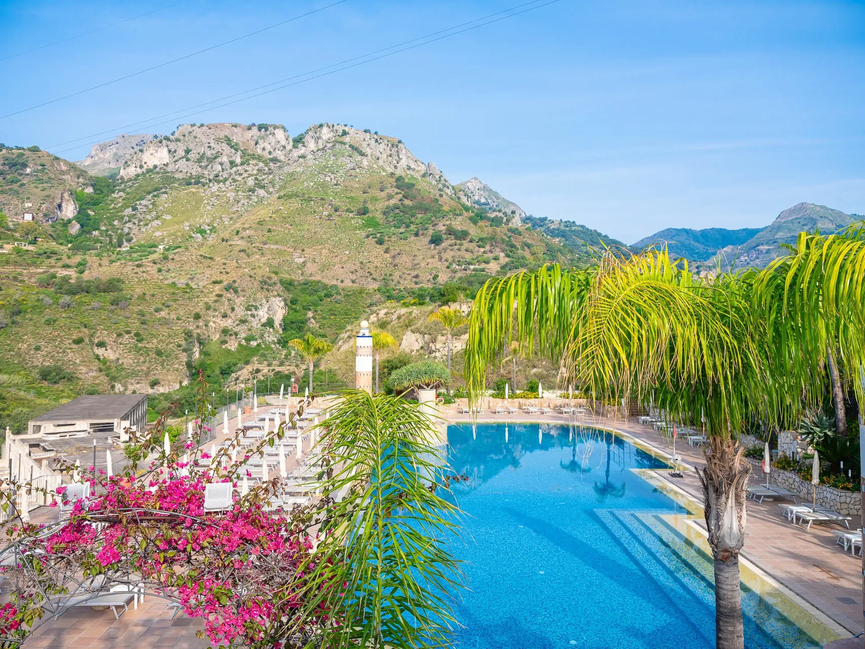 Piscina con lettini e palme e montagne verdi sullo sfondo
