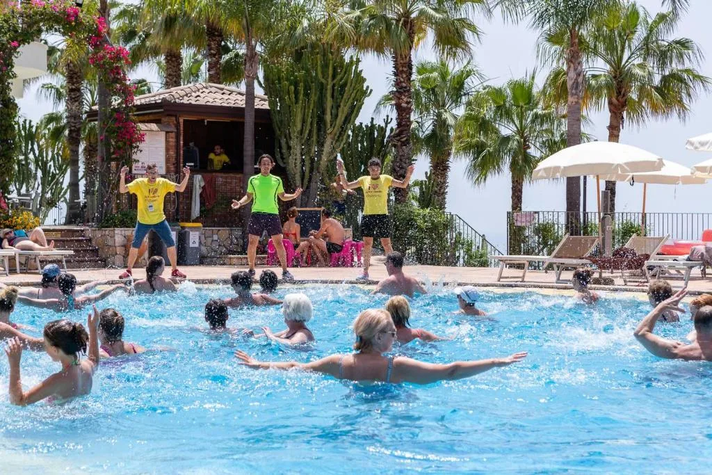 Attività di acquagym in piscina con animatori e ospiti tra le palme