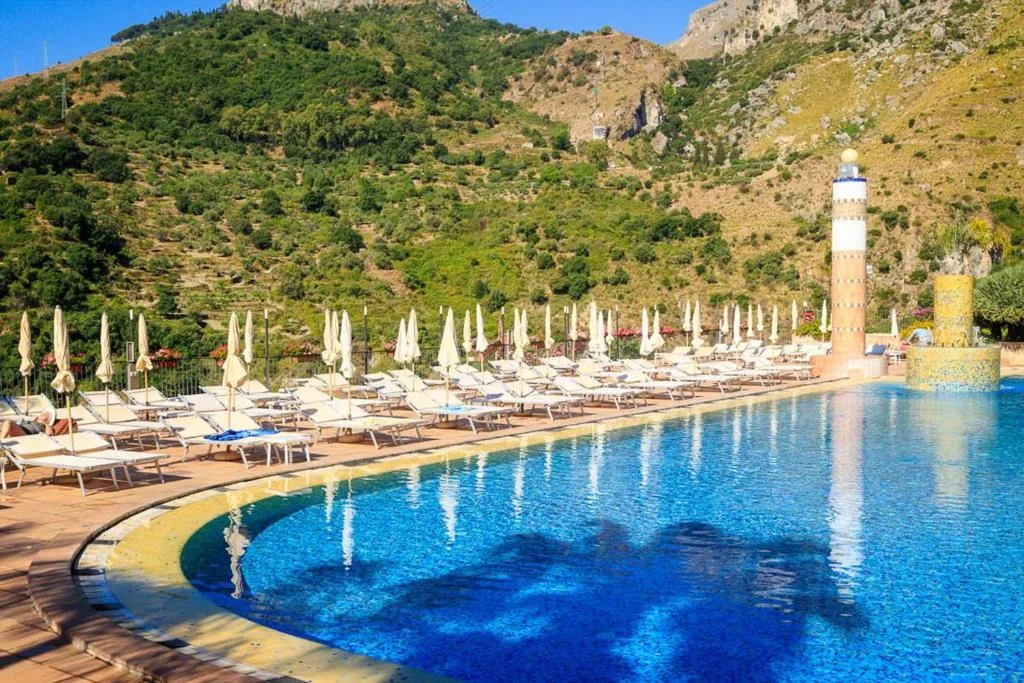 Piscina esterna con lettini, ombrelloni e montagne sullo sfondo