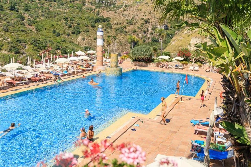 Piscina animata con ospiti in acqua e lettini circondata dalla natura