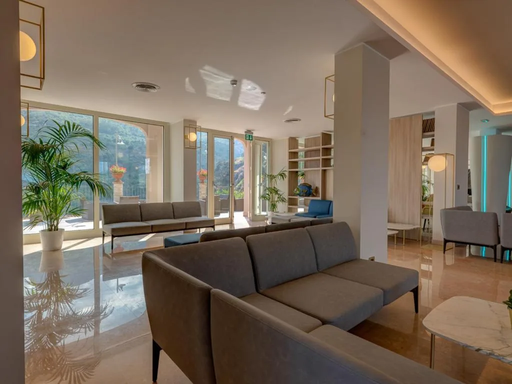 Salone interno con divani grigi, piante e grandi vetrate sulla terrazza