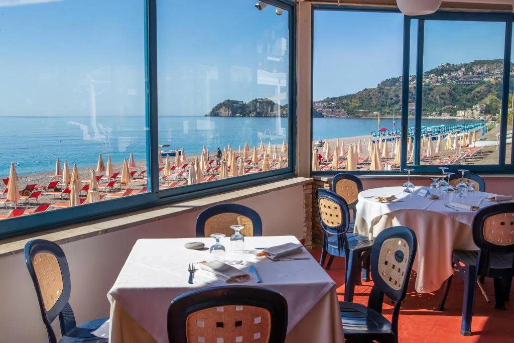 Sala ristorante con tavoli apparecchiati e grandi finestre sulla spiaggia