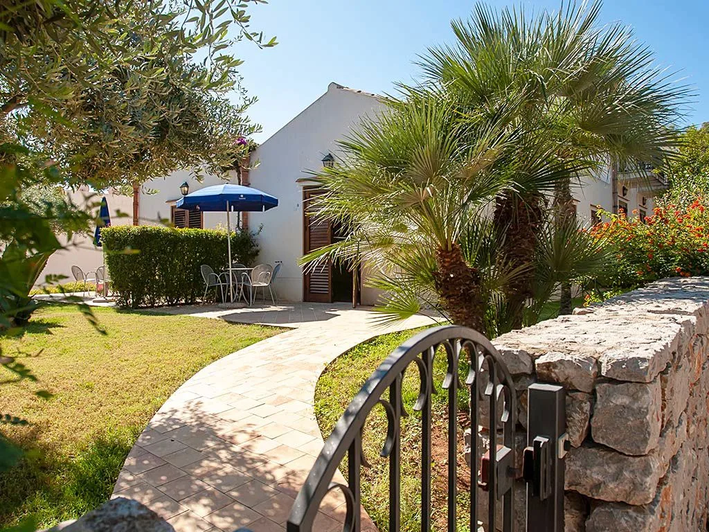 Giardino fiorito con vialetto e bungalow bianco con ombrellone