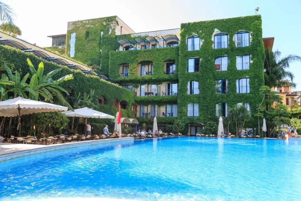 Piscina esterna con edificio dell'hotel ricoperto di edera e area lounge con ombrelloni bianchi