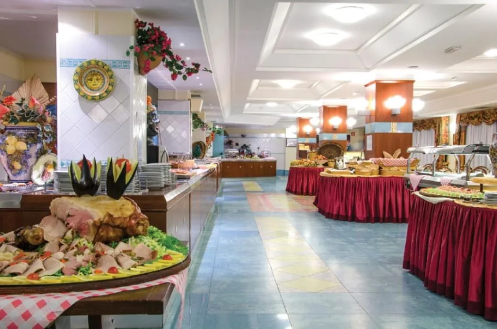Buffet del ristorante con piatti di carne, dolci e specialità esposte su tavoli con tovaglie rosse