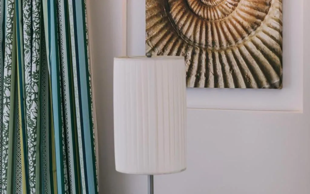 Dettaglio d'arredo con lampada, tende a righe e quadro con conchiglia