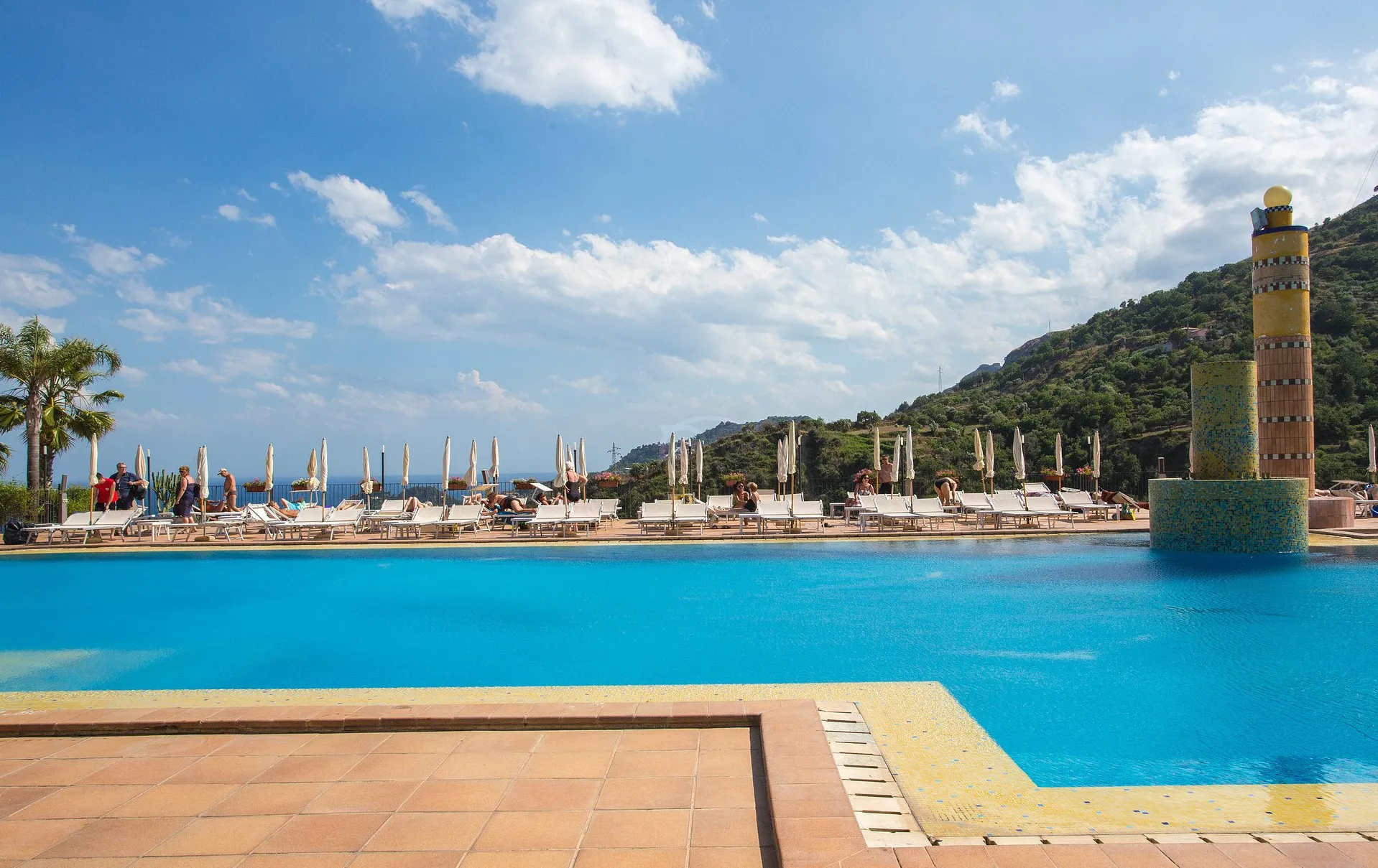 Piscina con lettini e ombrelloni sotto un cielo azzurro con nuvole