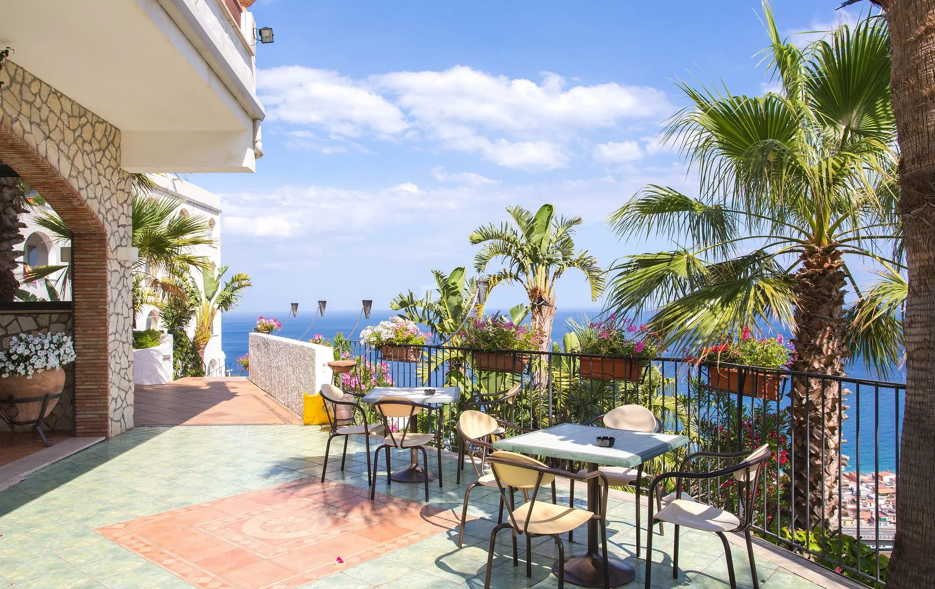 Terrazza esterna con tavoli, sedie e palme affacciata sul mare