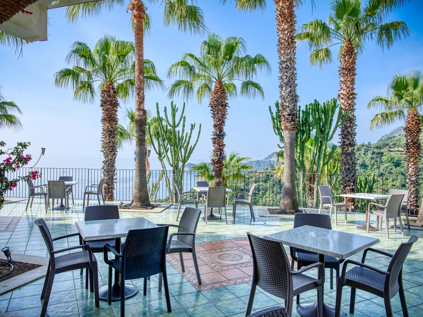 Terrazza con tavoli, palme e cactus affacciata sul mare
