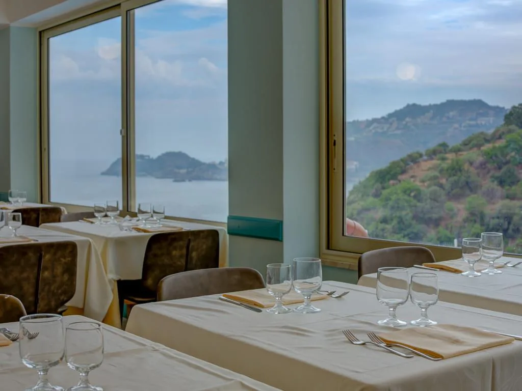Ristorante con tavoli apparecchiati e finestre panoramiche sul mare e colline