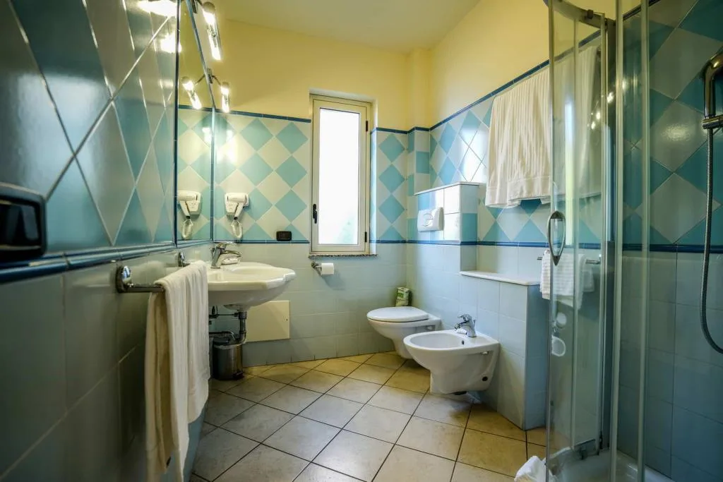 Bagno luminoso con piastrelle azzurre, lavabo, bidet, wc e doccia con finestra
