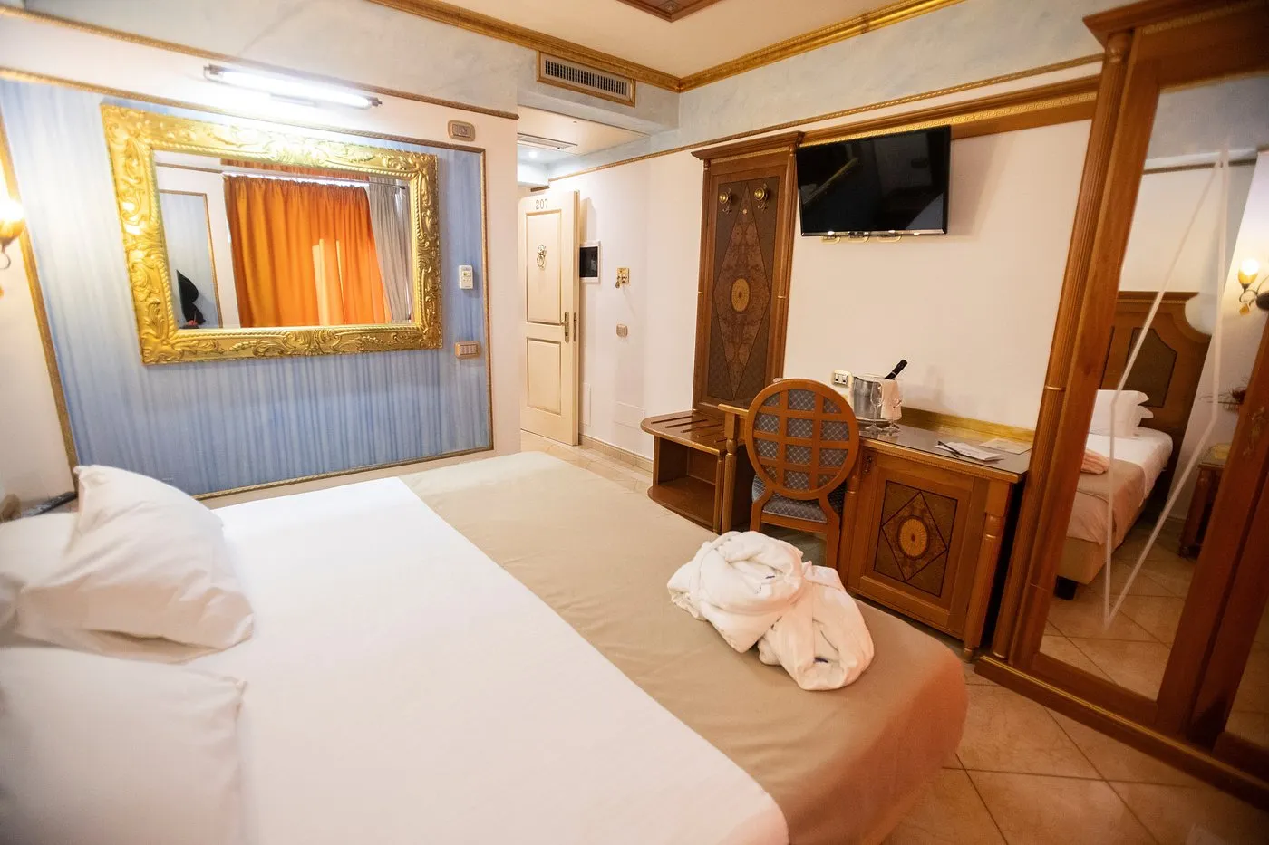 Camera con letto, scrivania in legno intarsiato, TV e grande specchio dorato