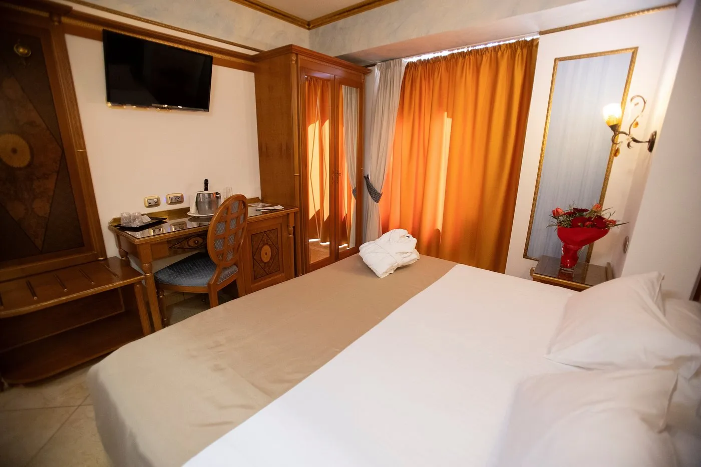 Camera con letto matrimoniale, scrivania in legno, TV e tende arancioni
