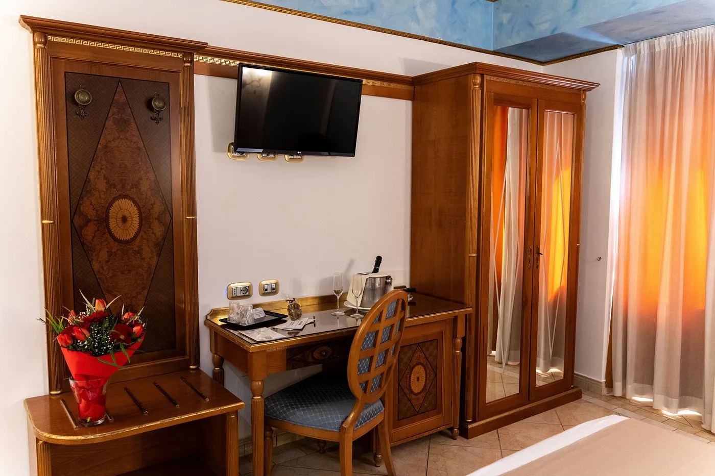 Dettaglio camera con scrivania in legno, TV a parete e fiori decorativi