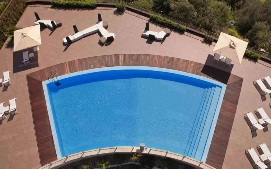 Vista dall'alto della piscina esterna con solarium in legno, lettini e ombrelloni