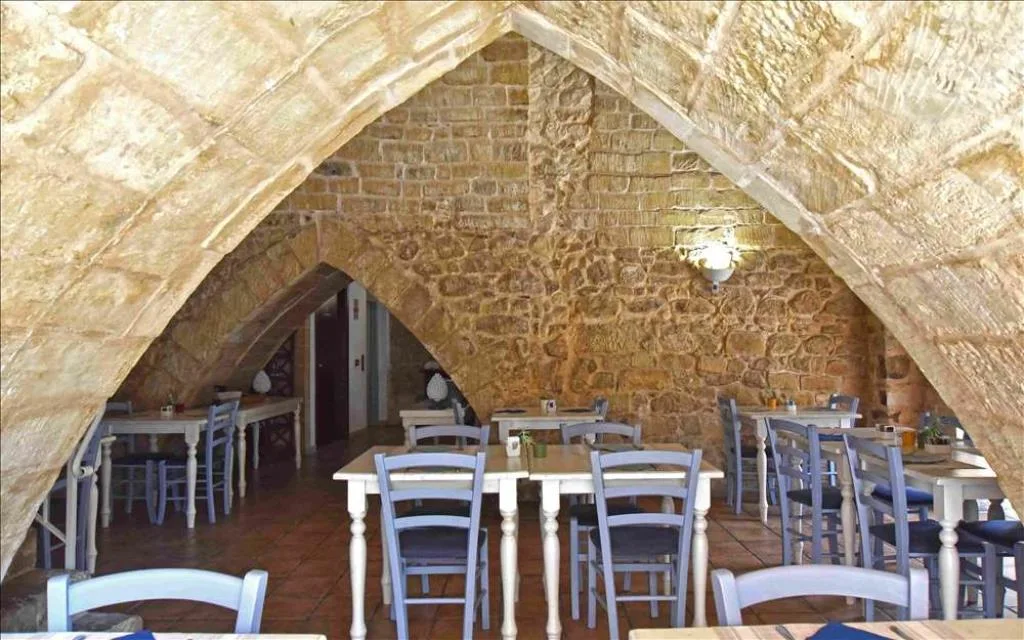 Sala ristorante con soffitto a volta in pietra e tavoli con sedie bianche e azzurre