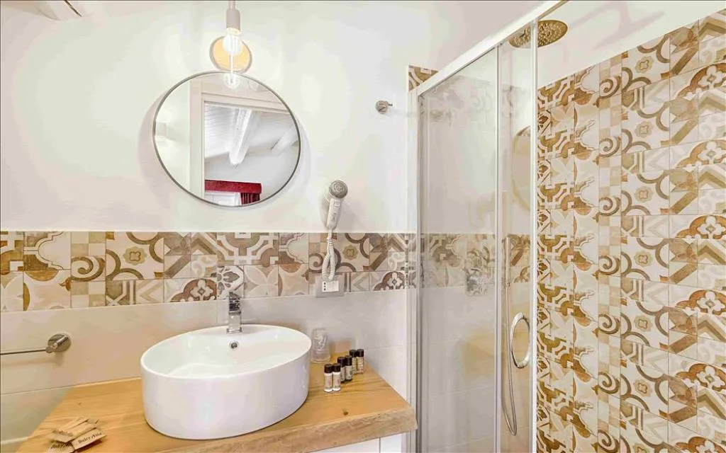 Bagno con lavabo tondo, specchio circolare, doccia in vetro e piastrelle decorate