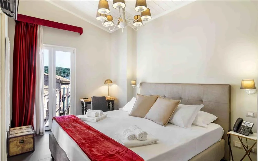 Camera matrimoniale elegante con tende rosse, lampadario e balcone con vista sulla città