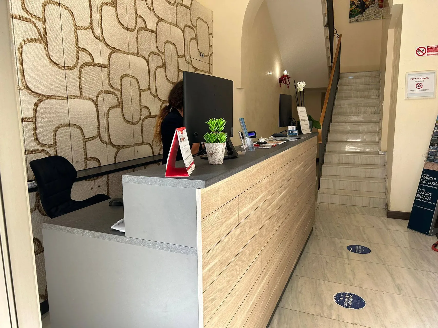 Reception dell'hotel con bancone in legno, addetta e scala in marmo sul lato