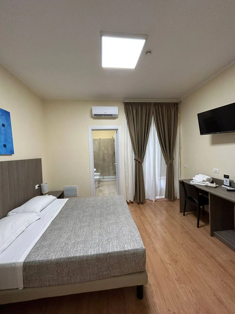 Camera doppia con bagno privato, scrivania, TV a parete e ampia finestra con tende