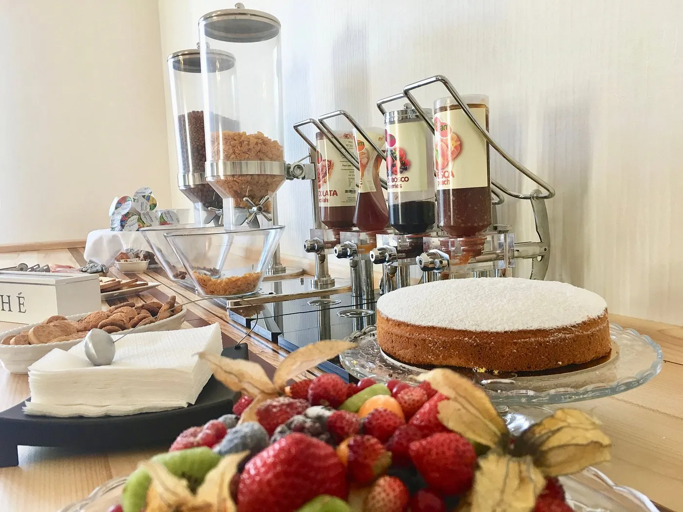 Buffet colazione con dispenser di cereali e marmellate, torta, frutta fresca e biscotti