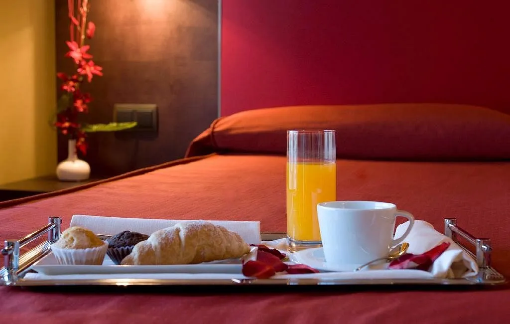 Colazione in camera servita su vassoio con cornetto, succo d'arancia e caffè su letto rosso