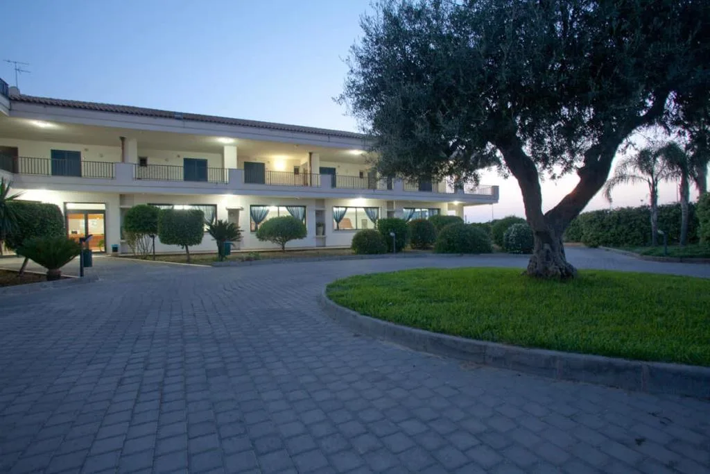 Esterno dell'hotel al tramonto con cortile pavimentato e ulivo