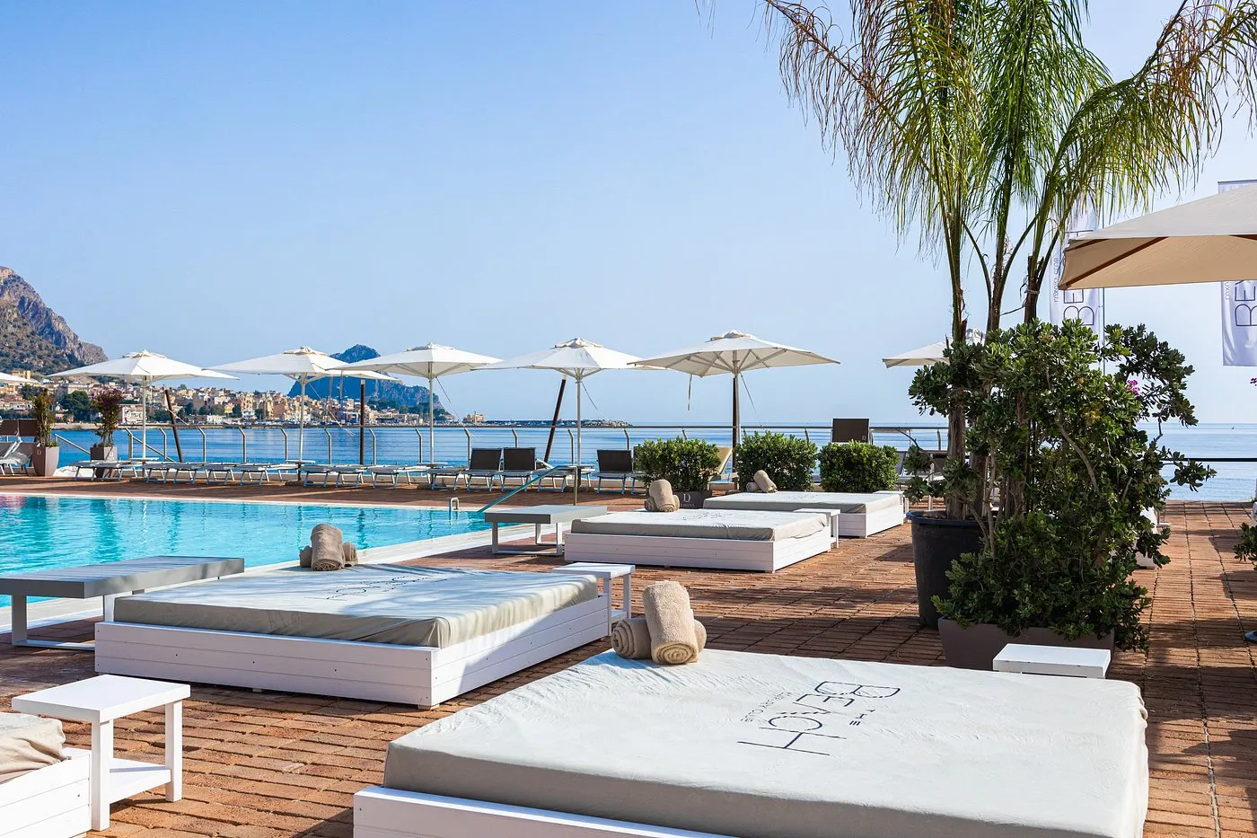 Terrazza solarium con lettini bianchi, ombrelloni e vista sul mare e sulla città costiera