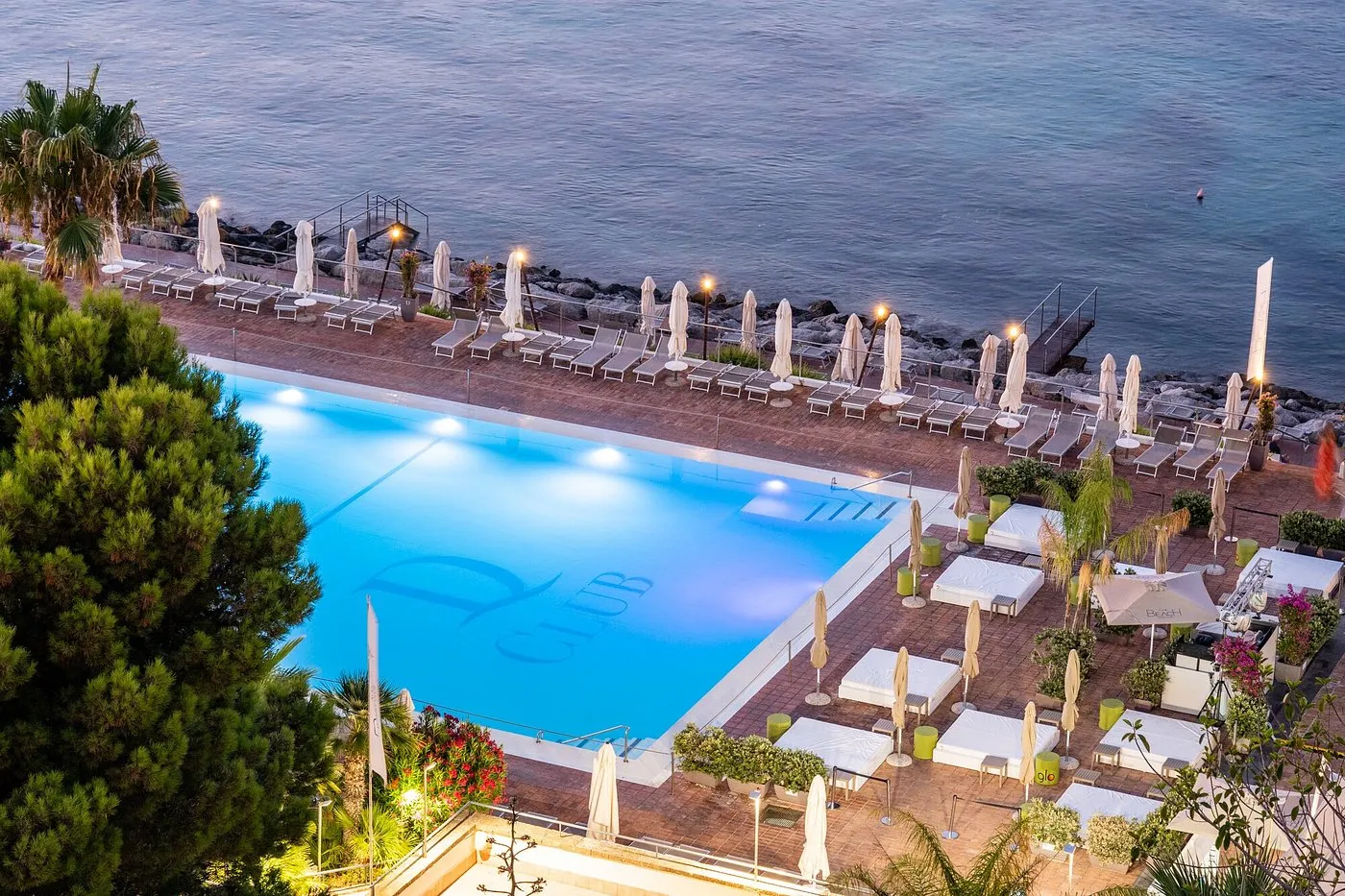 Vista dall'alto della piscina sul mare con lettini, ombrelloni e gazebo bianchi