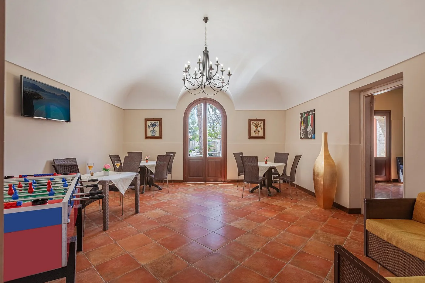 Sala giochi e relax con calcio balilla, tavoli, sedie e lampadario a candelabro