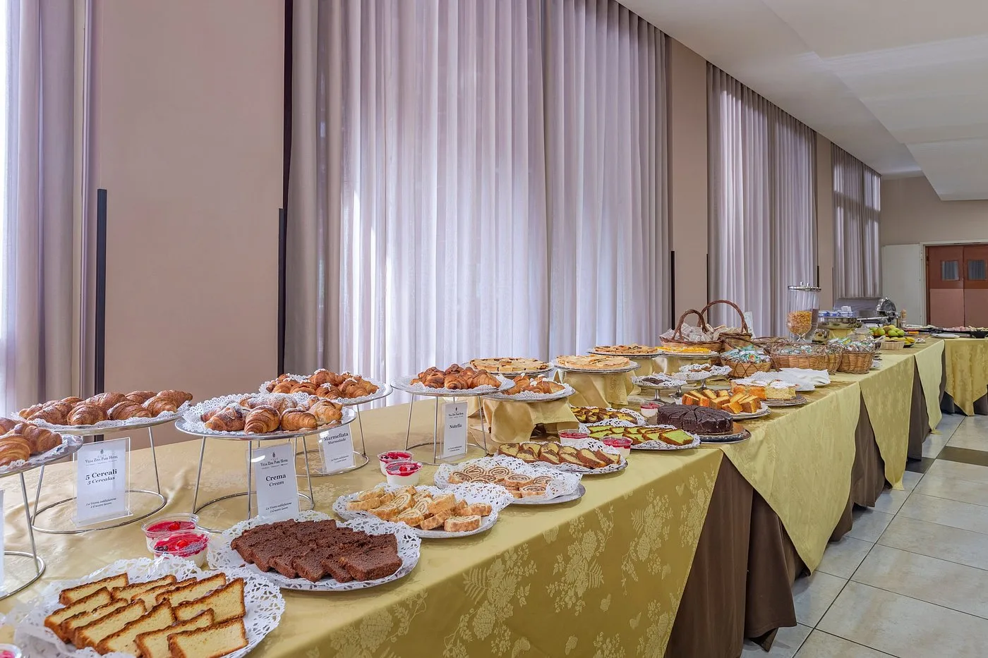 Buffet della colazione con cornetti, torte, dolci e cesti di pane su tavolo con tovaglia gialla