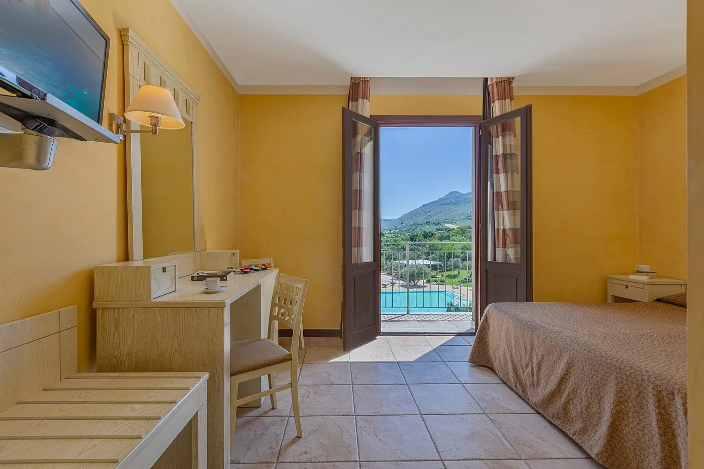 Camera con scrivania, TV e porta finestra affacciata su piscina e montagne