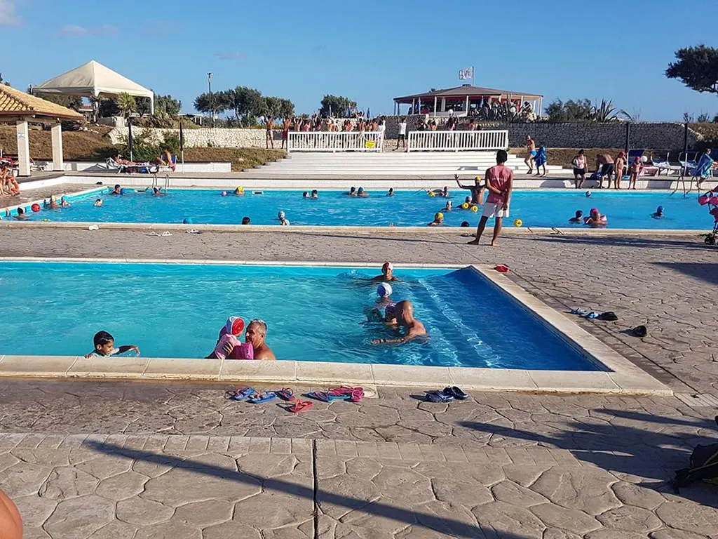 Area piscine con bagnanti, vasca per bambini e gazebo sullo sfondo