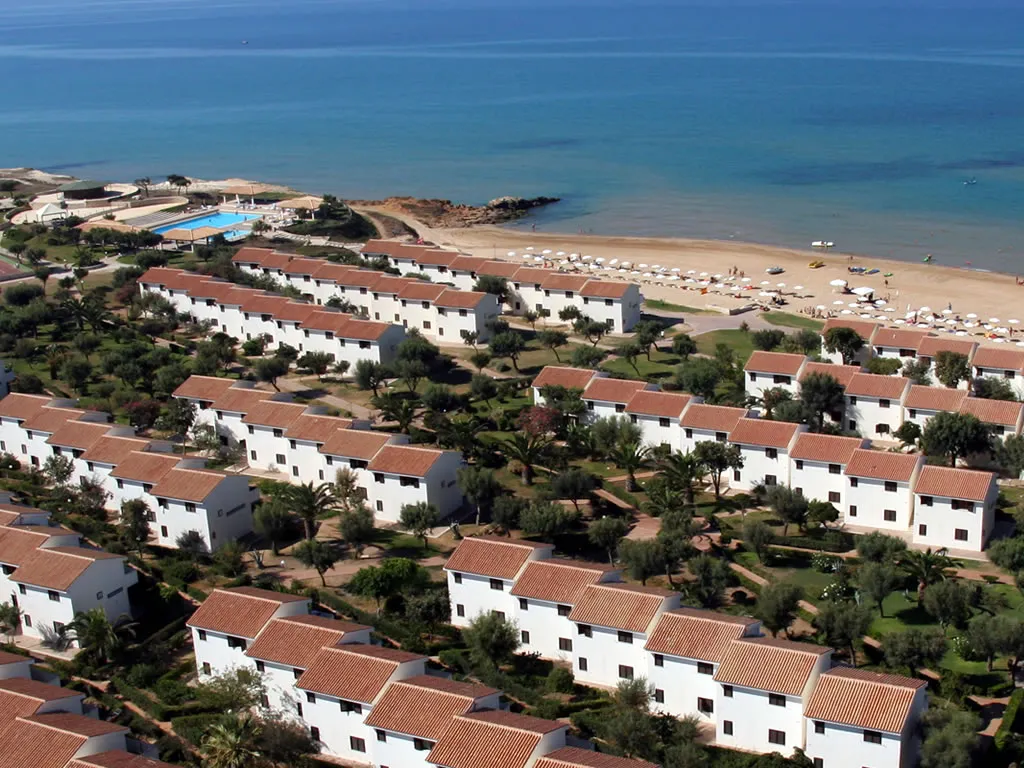 Vista aerea dei bungalow bianchi con tetti in coppi, giardini, piscina e spiaggia sul mare