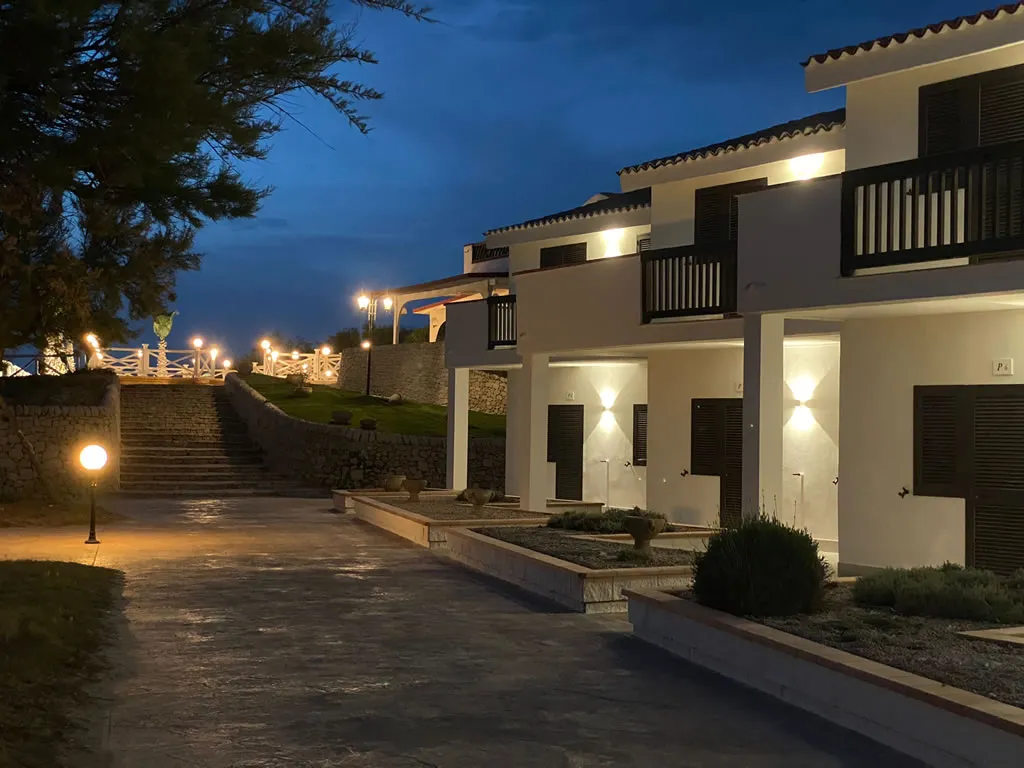 Edifici del resort illuminati di sera con vialetto e scalinata in pietra