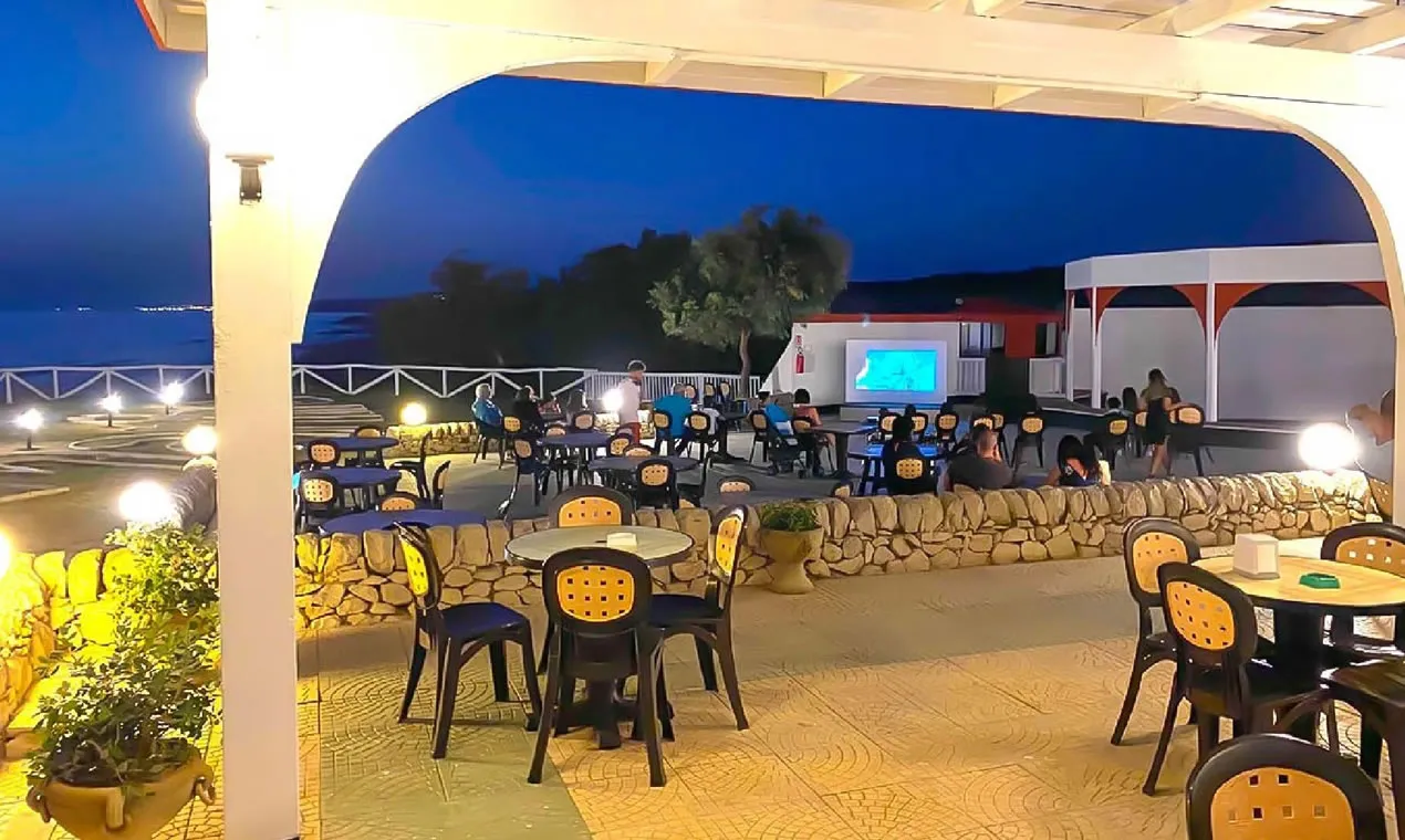 Terrazza serale con tavoli, ospiti e schermo per proiezioni vista mare