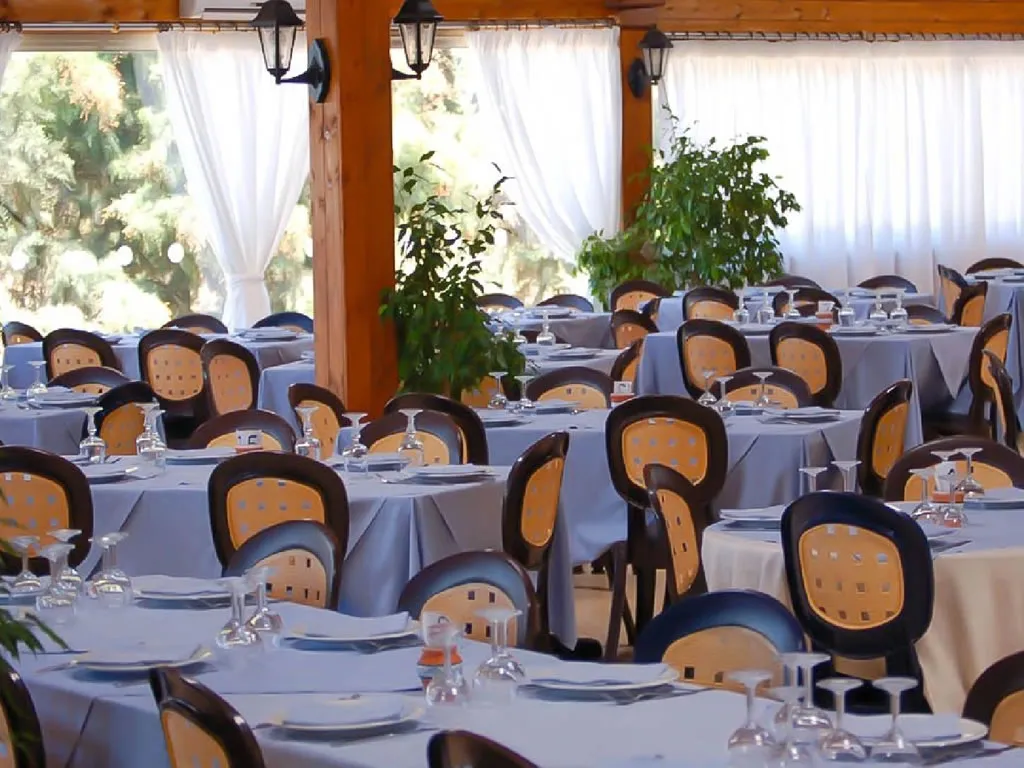 Sala ristorante interna con tavoli apparecchiati e ampie vetrate sul verde