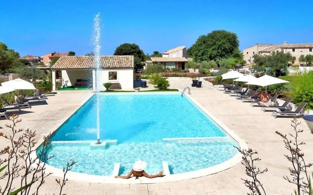 Piscina esterna con fontana a zampillo, lettini e ombrelloni bianchi