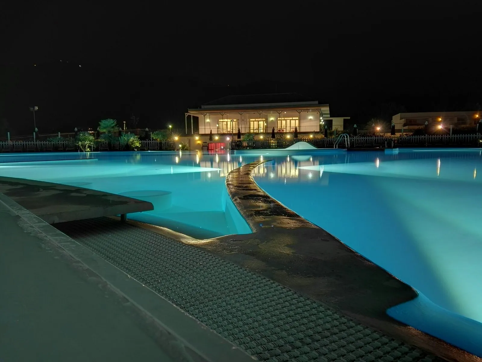 Piscina illuminata di notte con riflessi luminosi e ristorante sullo sfondo