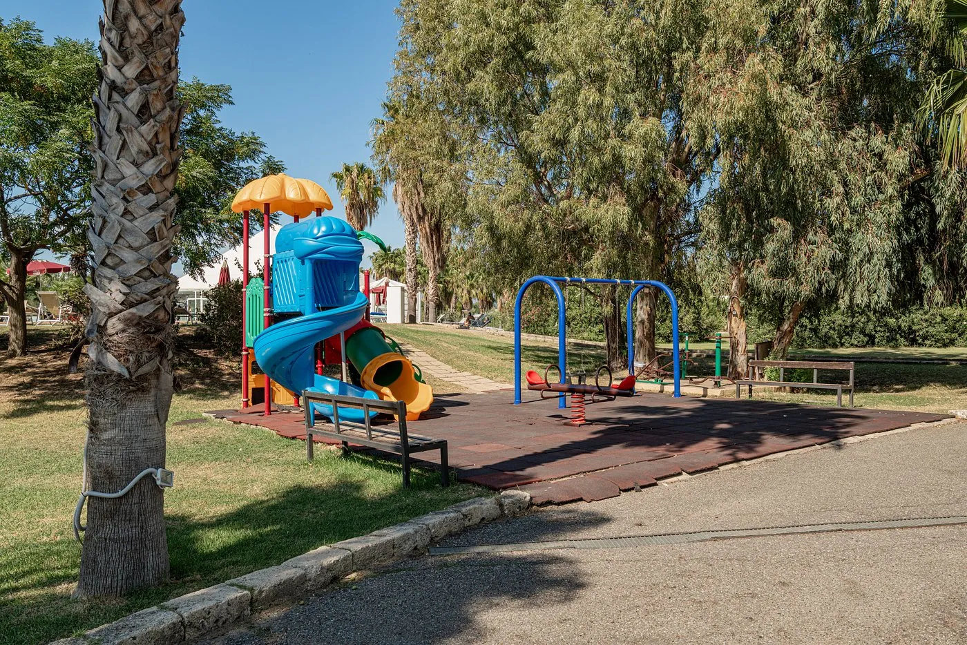 Area giochi per bambini all'aperto con scivolo colorato e altalene tra le palme
