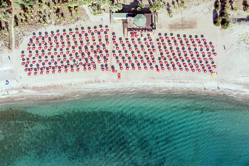 Vista aerea della spiaggia con ombrelloni rossi e neri e mare cristallino