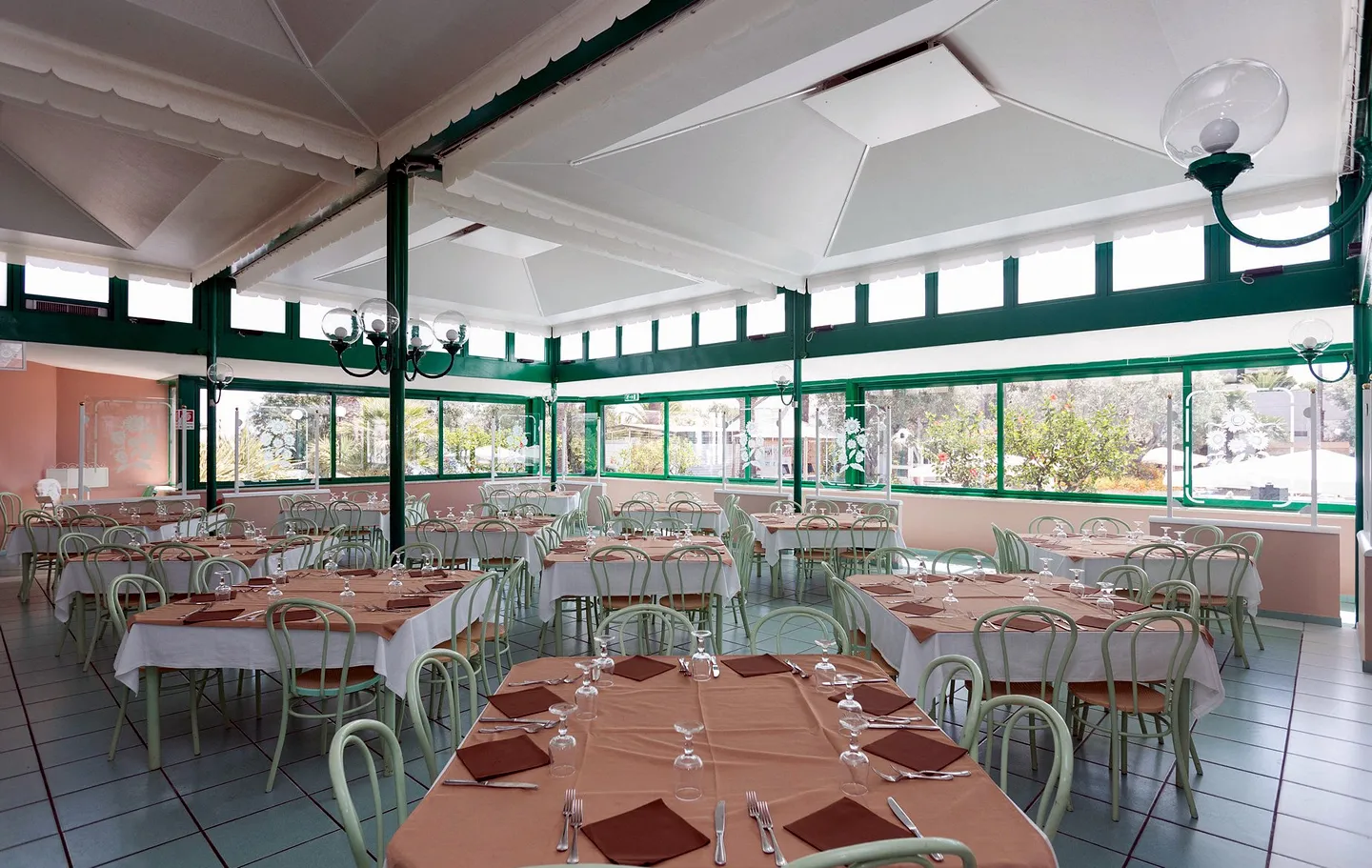 Sala ristorante interna con tavoli apparecchiati, tovaglie e ampie vetrate sul giardino