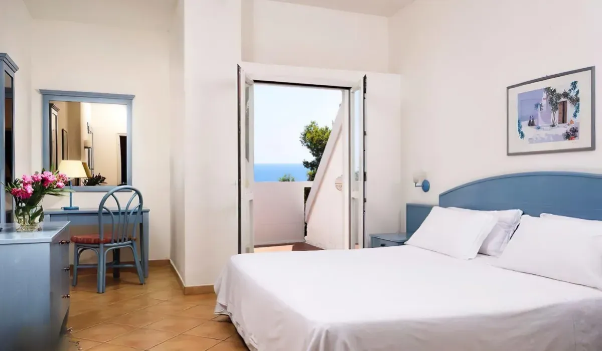 Camera con letto matrimoniale, arredi azzurri e porta finestra con vista mare