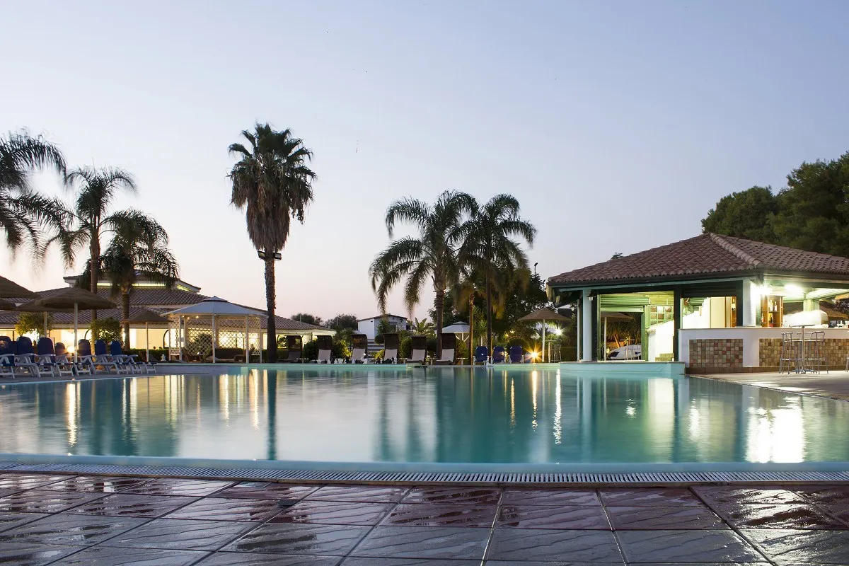 Piscina del resort al tramonto con palme e bar illuminato