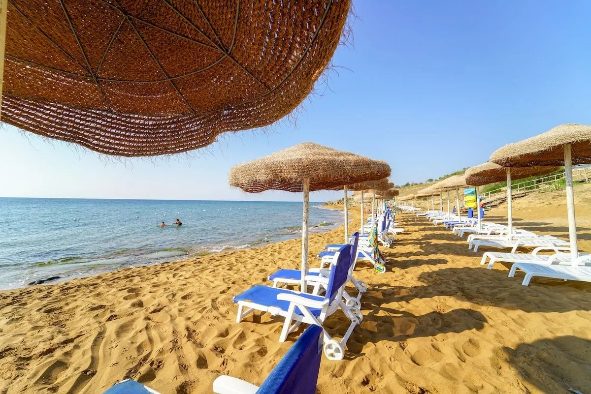 Spiaggia di sabbia dorata con ombrelloni in paglia e lettini blu sul mare