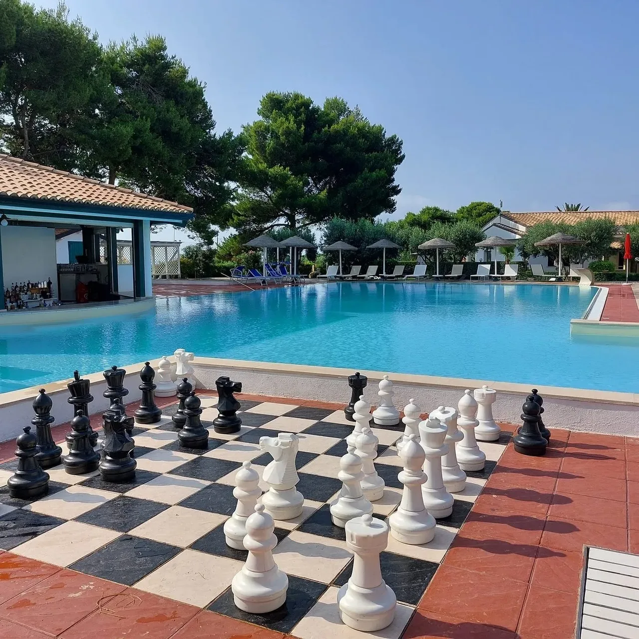 Bordo piscina con scacchiera gigante e bar in una giornata soleggiata