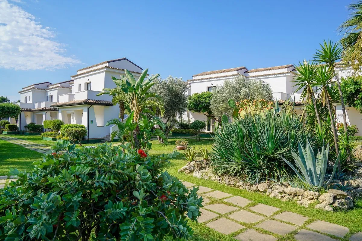 Giardino curato con piante mediterranee e villette bianche del resort