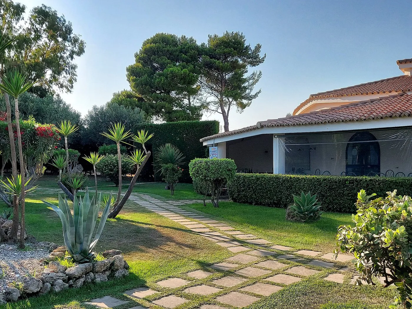 Giardino con vialetto in pietra, piante mediterranee e edificio del resort